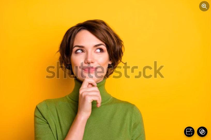 A woman in a green turtleneck stands against a bright yellow background, looking up thoughtfully with her finger resting on her chin, suggesting she is thinking or pondering.